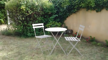 En liten sittplats utomhus med två metallstolar och ett runt bord, omgiven av gräs och grönska.