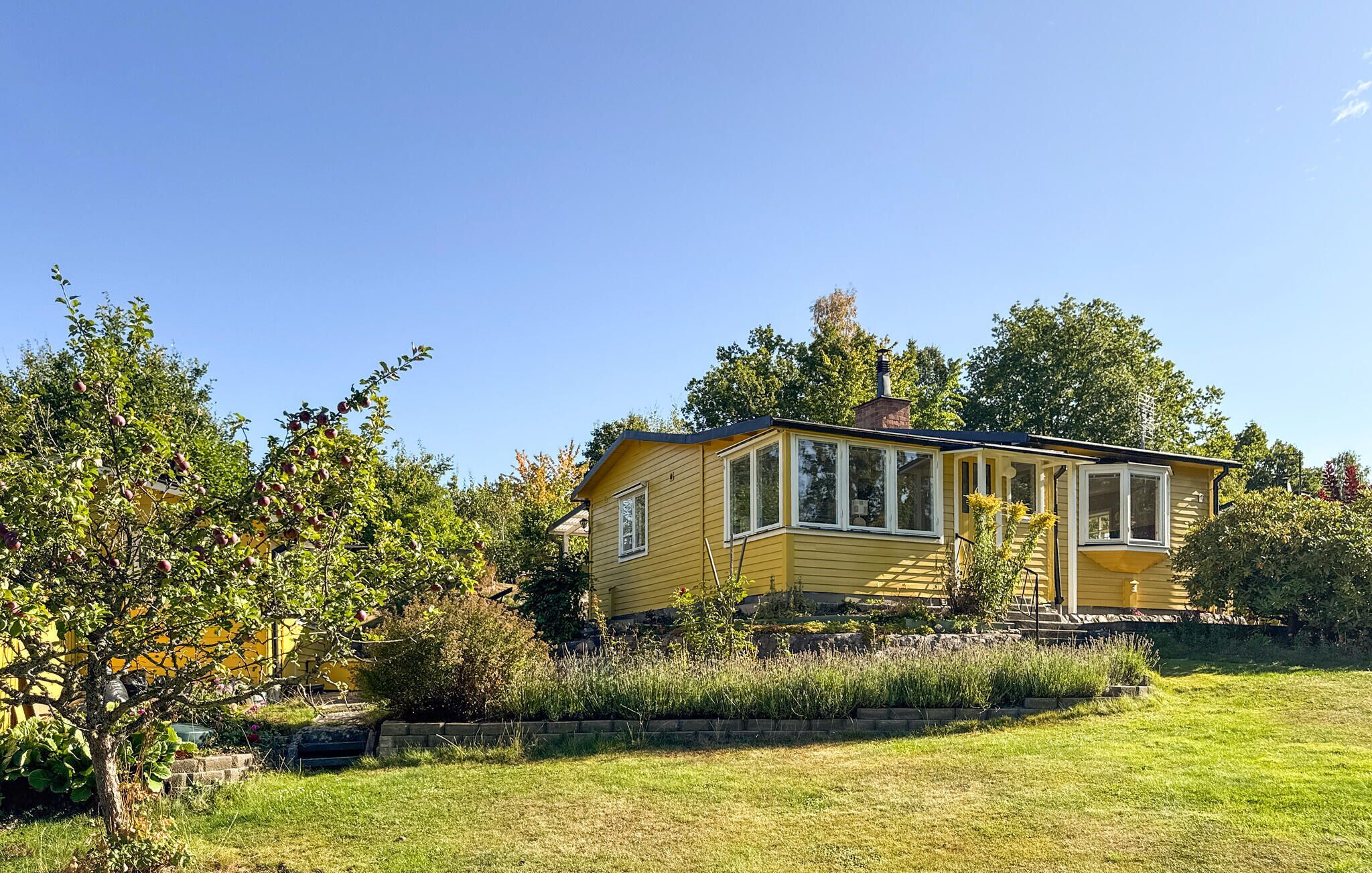 Une maison jaune avec un porche, entourée d’une cour verdoyante et d’arbres.