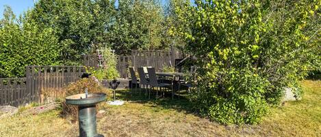 Un jardin avec une clôture en bois, une mangeoire à oiseaux en métal et une table avec des chaises.