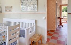 Ett rum med en spjälsäng, en liten pall, ett bord med ett blommigt bordsduk, en tavla som hänger på väggen och ett mönstrat golv.