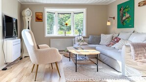 A living room with a sofa, armchair, coffee table, and a large window with a view of greenery. - Cozy home in Bestorp with WiFi (Bestorp)