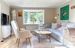 Ett vardagsrum med en soffa, fåtölj, soffbord och ett stort fönster med utsikt över grönområden.