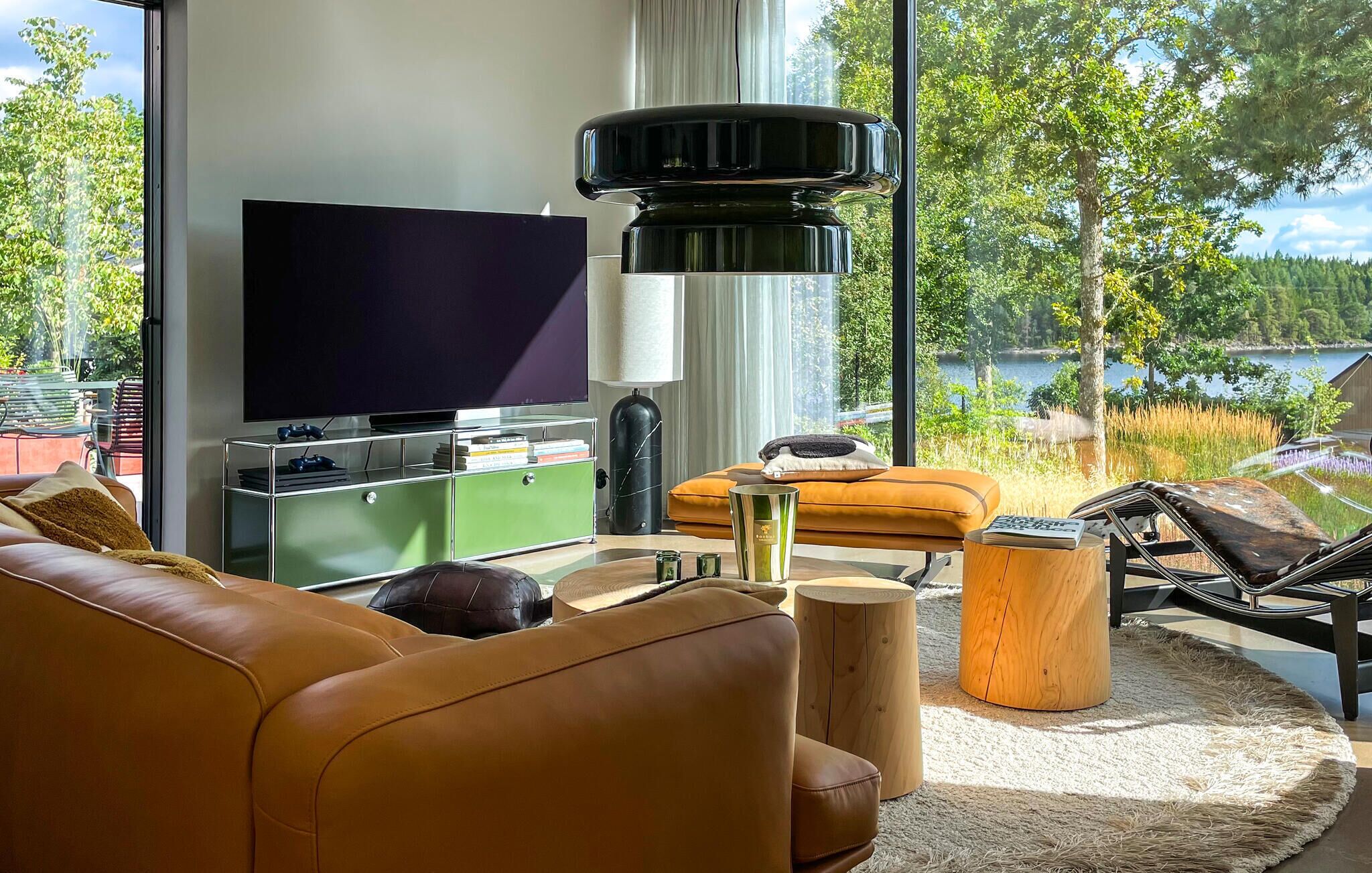 Un salon moderne doté d’un grand téléviseur à écran plat, d’un meuble vert, d’un canapé jaune et offrant une vue sur un lac.