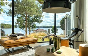 Uma sala de estar moderna com vista para um lago, um sofá de couro, uma cadeira de metal e uma mesa de madeira redonda com velas.