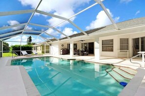 Ein überdachter Pool mit blauem Himmel darüber, umgeben von einem weißen Gebäude mit Terrasse.