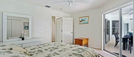 A bedroom with a bed, a ceiling fan, a door, a small table, and a view through a glass door.