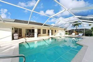 A swimming pool with a glass ceiling, lounge chairs, and a covered outdoor seating area. - CCVS - Villa Allegra (Cape Coral)