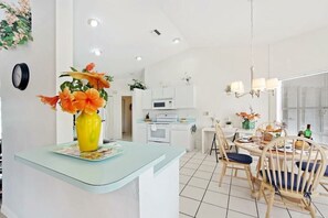 Une cuisine moderne avec des meubles blancs, un four à micro-ondes et un coin repas comprenant des chaises et une table en bois.