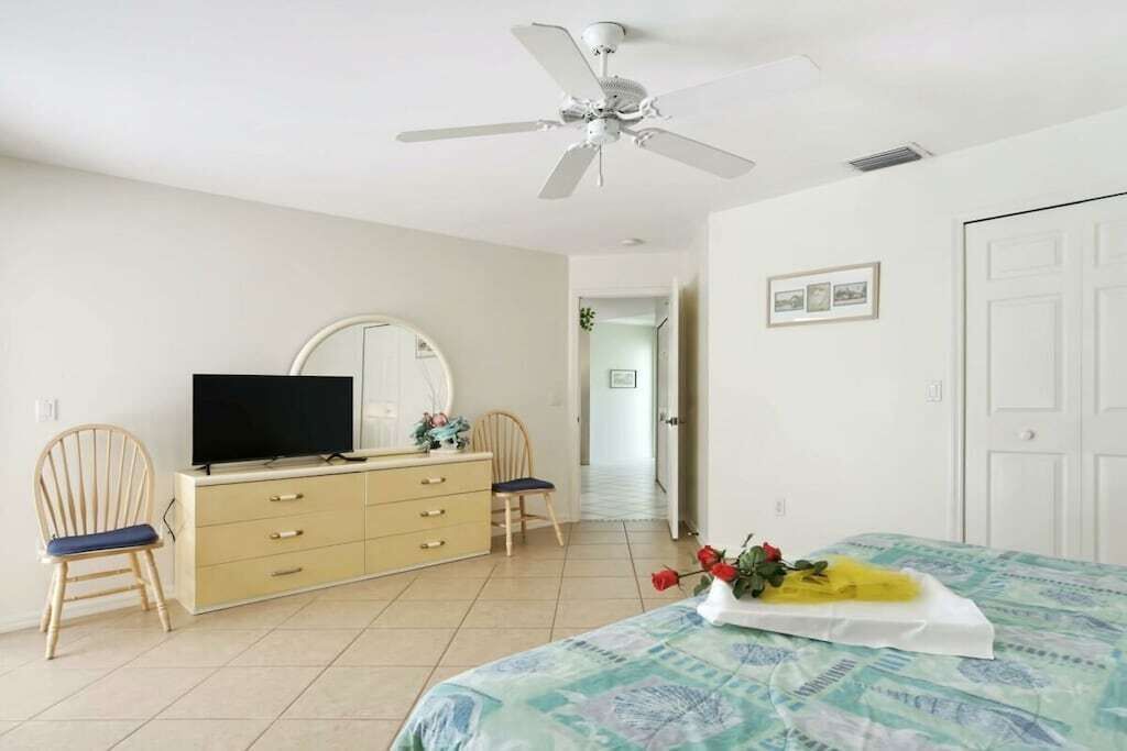 A room with a bed, a television on a dresser, a ceiling fan, and a door.