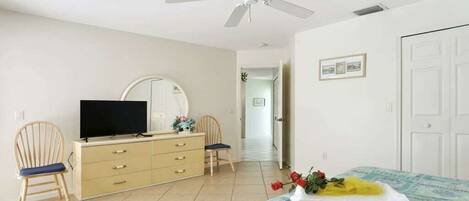 A room with a bed, a television on a dresser, a ceiling fan, and a door.