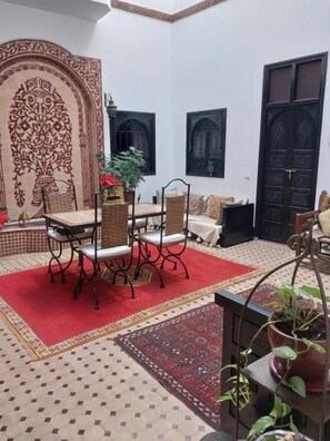 A traditional Moroccan interior with a patterned floor, a red rug, a table with chairs, and a large decorative arch. - Riad Dar Zampa (Marrakech)