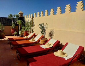 A terrace with sun loungers, potted plants, and a decorative wall. - Riad Dar Zampa (Marrakech)