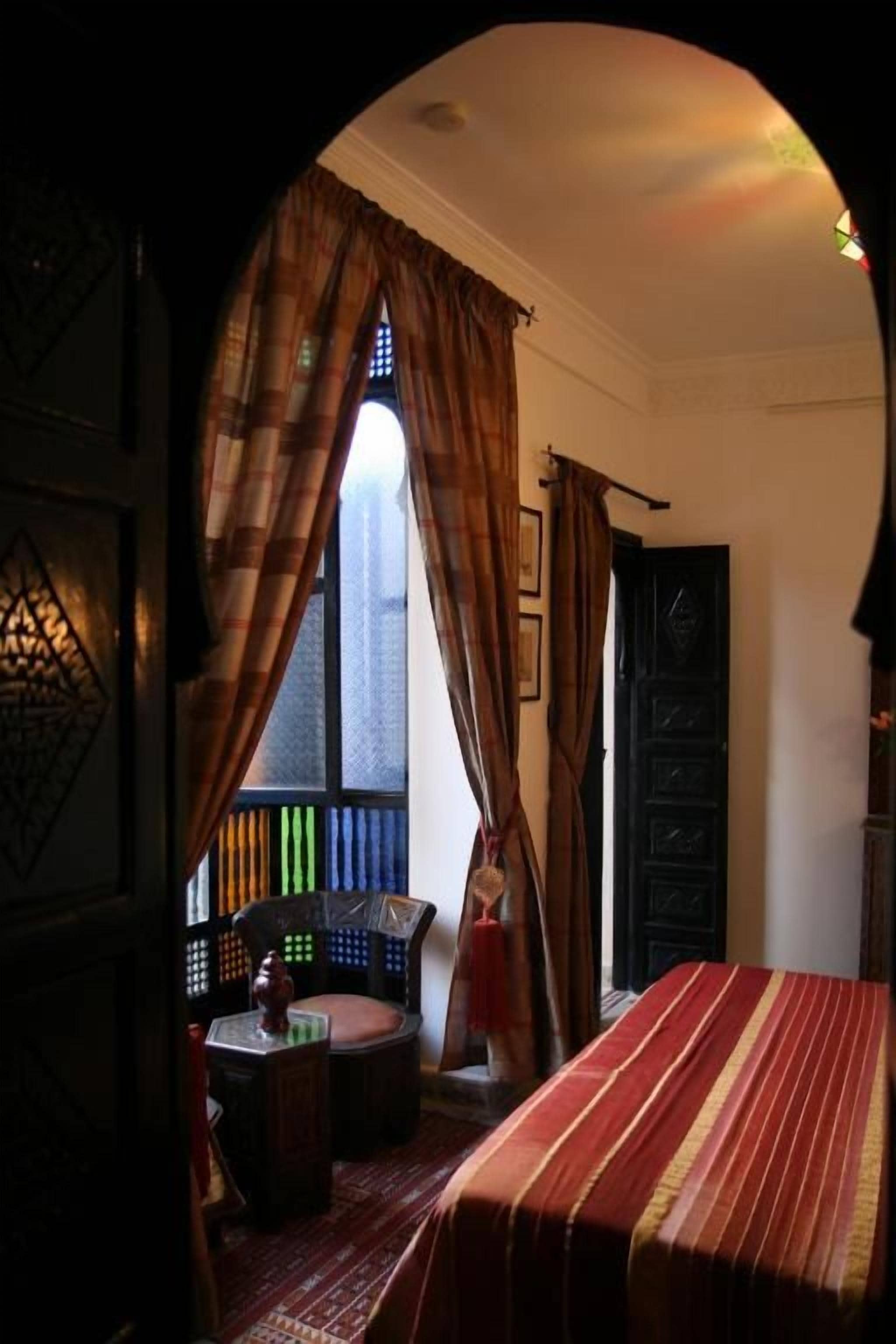 Une pièce avec un lit, une fenêtre avec des rideaux, une chaise et une petite table.