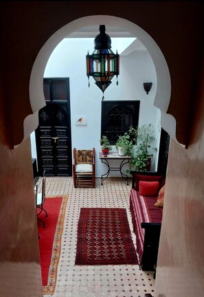 A room with a patterned floor, a wooden chair, a red sofa, a table with a plant, and a wall-mounted lamp. - Riad Dar Zampa (Marrakech)