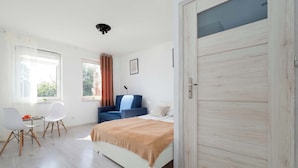 A bedroom with a bed, a desk, chairs, a window, and a door. - Cozy Apartment with Bedroom | Smart TV and Washing Machine (Łódź)