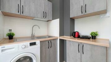 Una cocina compacta con armarios grises, lavadora y cafetera.