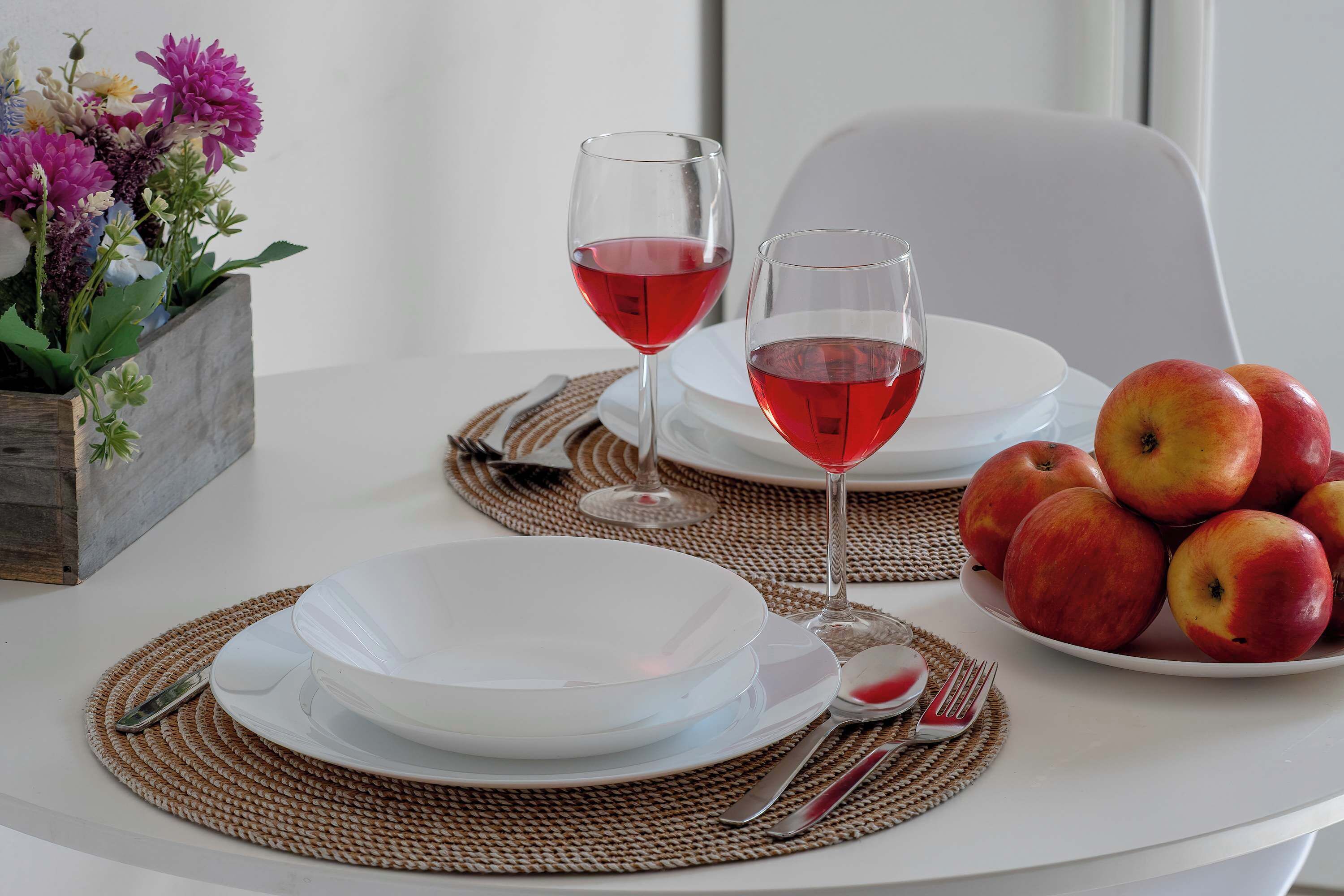 Ein Tisch mit zwei Weingläsern, einer Schale Äpfeln und einer Blumenvase.