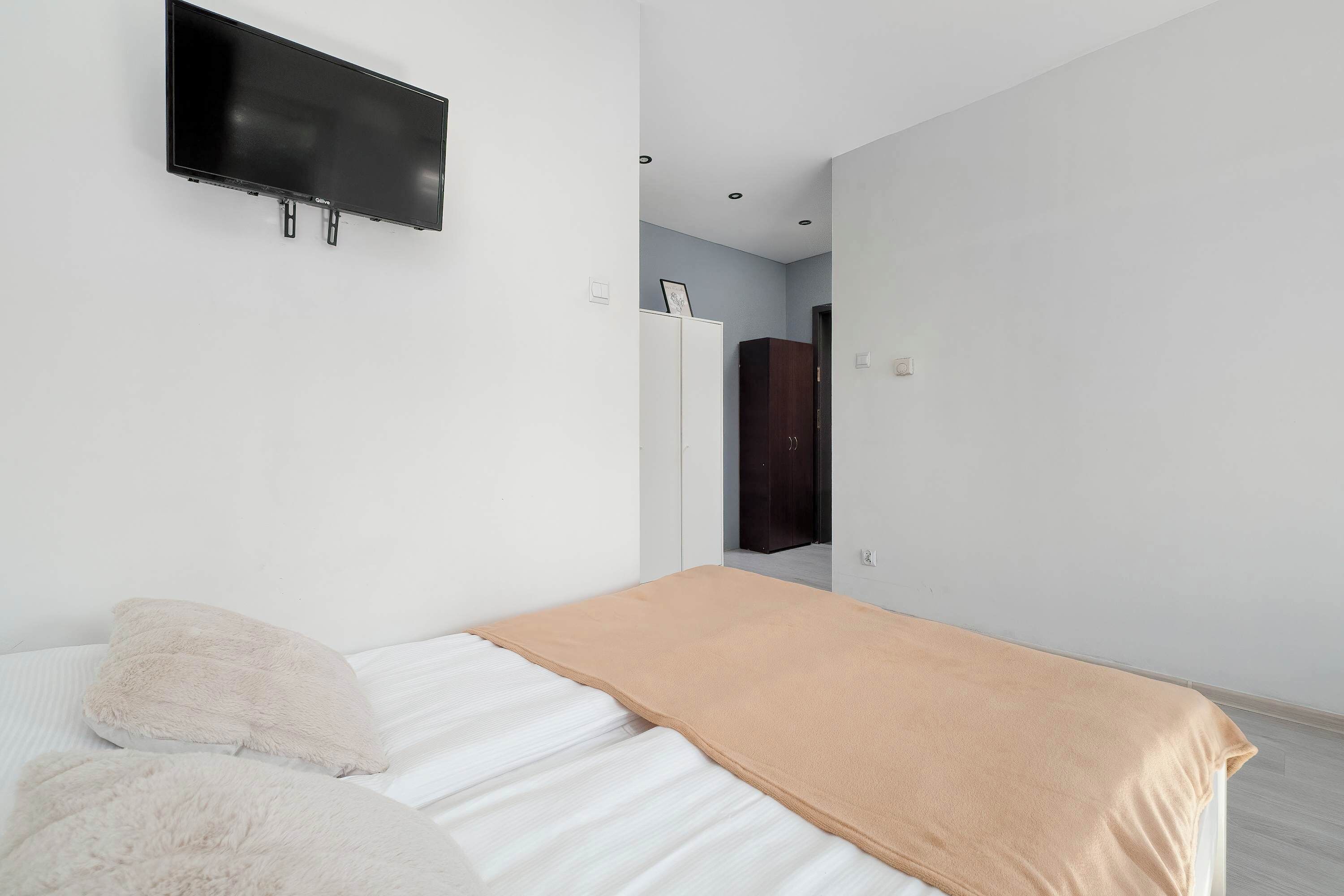 A bedroom with a bed, a television mounted on the wall, and a wardrobe.