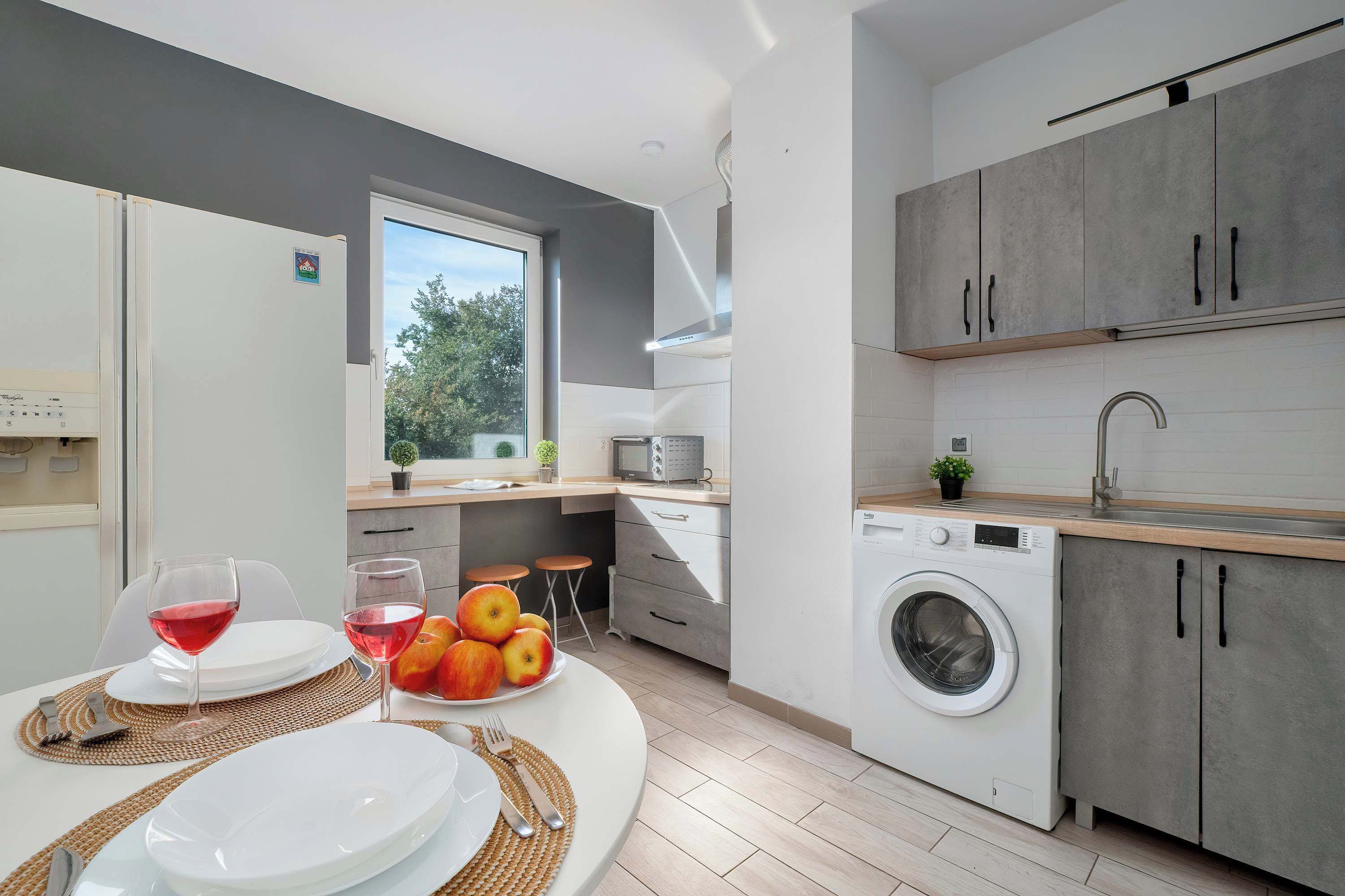 A modern kitchen with a built-in washing machine, a dining area with a table set for two, and a window providing a view of the outdoors.