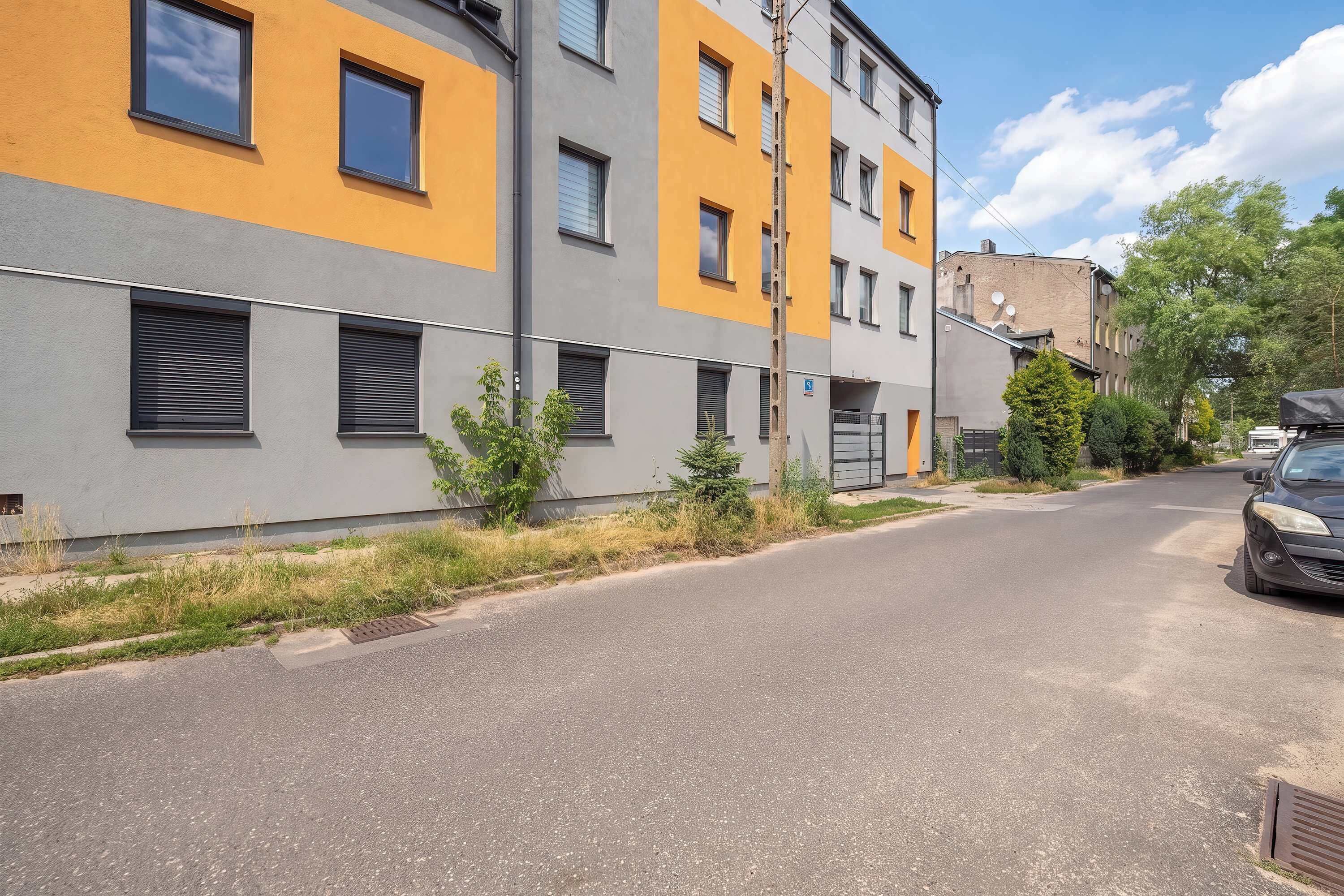 En boligbelagt gade med moderne bygninger, klar himmel og en parkeret bil.