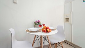 A small dining area with a white table, two white chairs, a glass of red wine, and a plate of apples. - Cozy Apartment with Bedroom | Smart TV and Washing Machine (Łódź)
