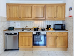 A kitchen with wooden cabinets, a dishwasher, an oven, a microwave, and a tiled backsplash. - Vacation home Albert by Interhome (Bad Staffelstein)