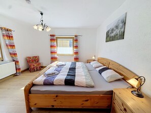 A bedroom with a wooden bed, a window with curtains, a nightstand, a chair, and a painting on the wall. - Vacation home Albert by Interhome (Bad Staffelstein)