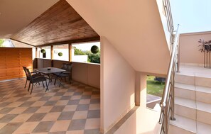 Een overdekt terras met een zwart-wit geruit vloertje, een eettafel met stoelen en uitzicht op groen.