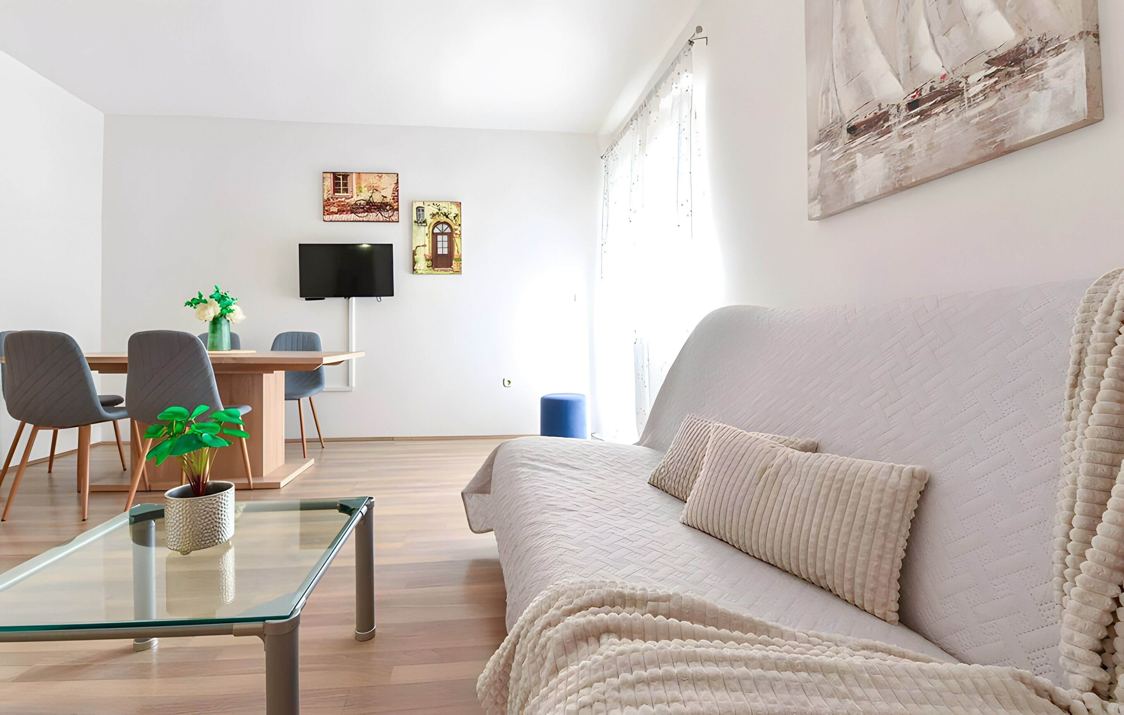 A modern living room with a sofa, a glass coffee table, and a dining area with chairs and a TV.