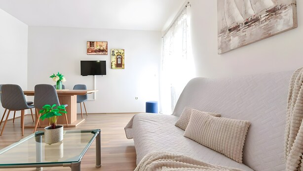 Una sala moderna con un sofá, una mesa de centro de vidrio y un área de comedor con sillas y un televisor.
