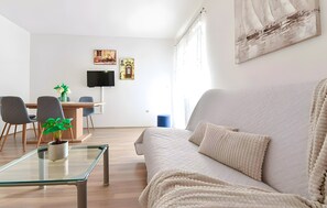 A modern living room with a sofa, a glass coffee table, and a dining area with chairs and a TV.