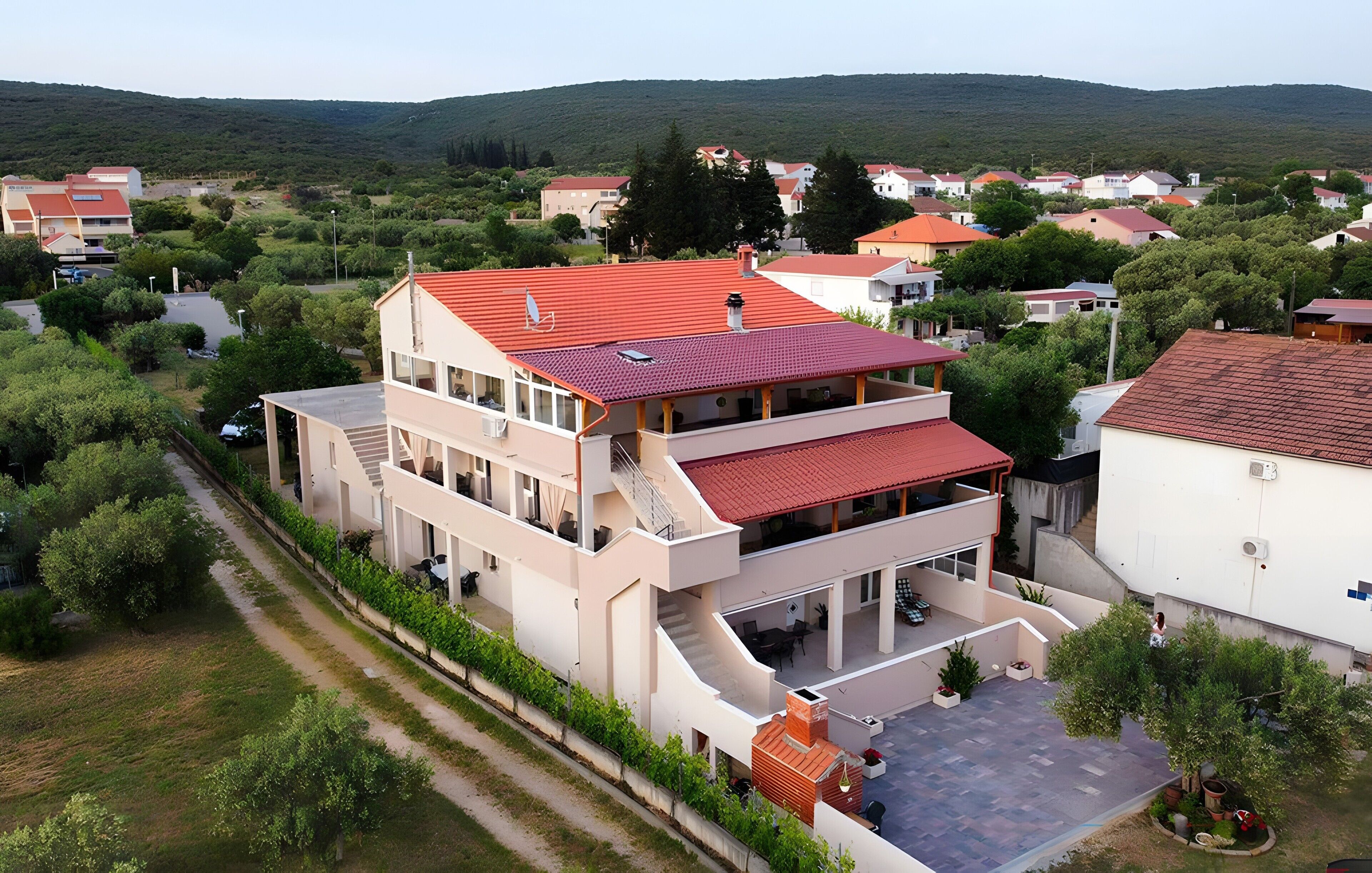 A multi-story residential building with a red roof, a covered outdoor area with seating, and a view of surrounding houses and greenery.