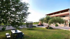 Un espacio exterior bien cuidado con un trampolín, una mesa con sillas y un edificio con tejado rojo.