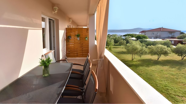 A balcony with a table and chairs, a wooden partition, and a view of a green landscape and buildings in the distance.