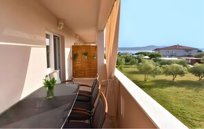 A balcony with a table and chairs, a wooden partition, and a view of a green landscape and buildings in the distance. - Apartment '3' with Sea View, Shared Terrace and Wi-Fi (Sveti Petar na Moru)