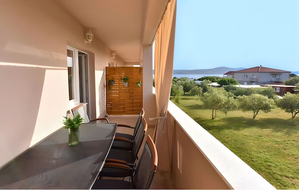A balcony with a table and chairs, a wooden partition, and a view of a green landscape and buildings in the distance.