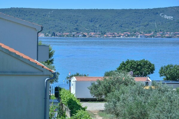 A coastal view with a body of water, a small building with a red roof, and a hillside in the background.