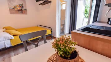 A modern hotel room with a bed, a small table, a plant, a TV, and a view of the outside.