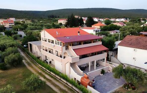 A multi-story residential building with a red roof, a covered outdoor area with seating, and a view of surrounding houses and greenery. - Apartment '6' with Sea View, Shared Terrace and Wi-Fi (Sveti Petar na Moru)