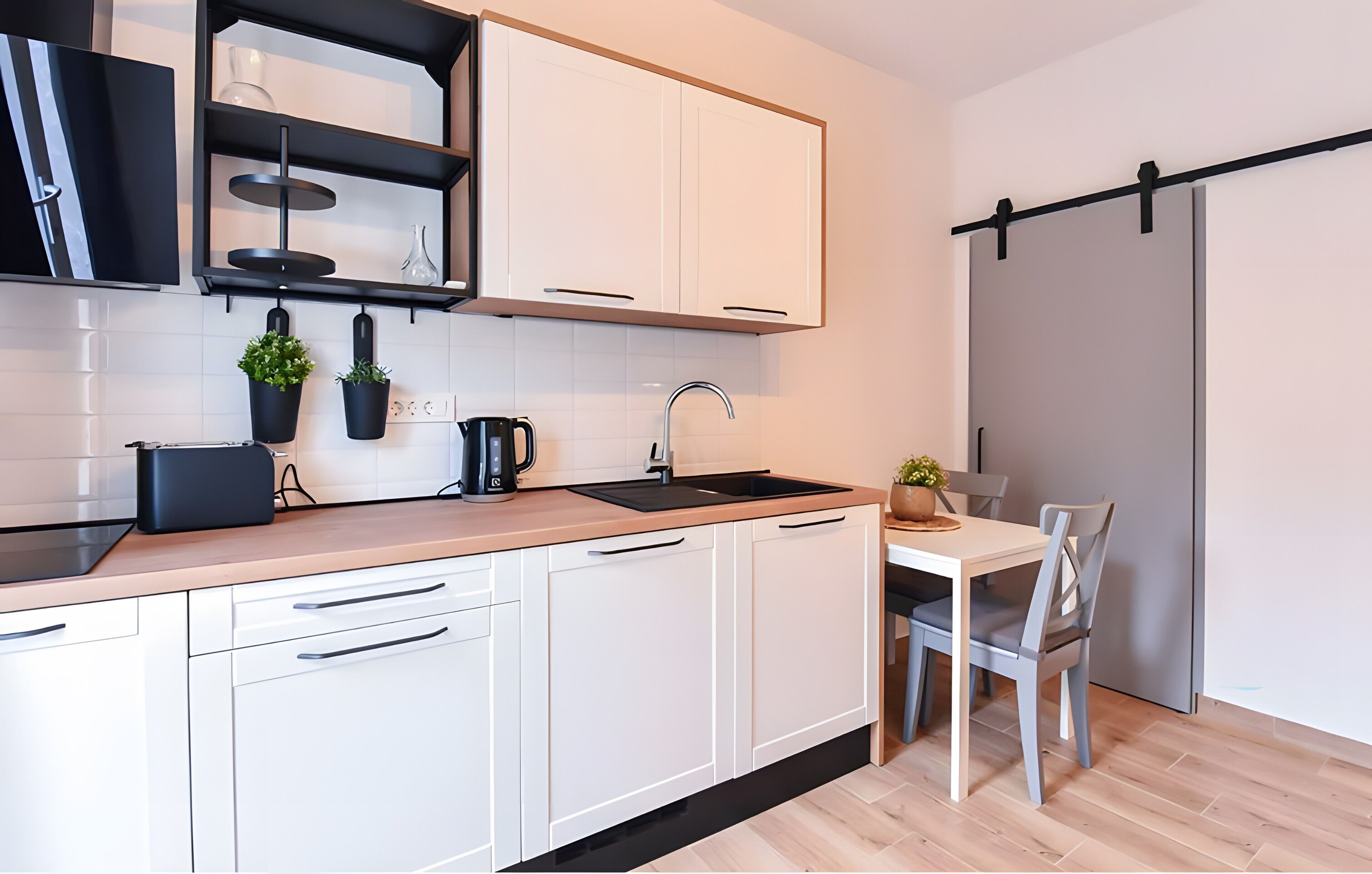 Une cuisine moderne avec des meubles blancs, un plan de travail noir, un évier et un coin repas comprenant une table et des chaises.