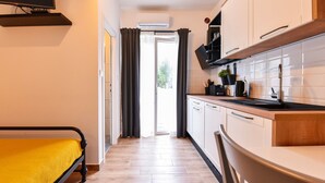 A compact kitchen with a dining area, a bed with a yellow cover, and a view through a door to an outdoor area.