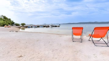 Una playa con dos sillas naranjas y una hilera de barcos al fondo.