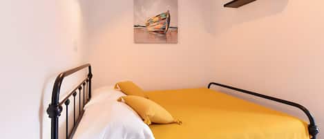 A single bed with a yellow bedspread and white pillows, a painting on the wall, and a mounted television.