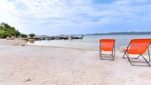 Una playa con dos sillas naranjas y una hilera de barcos al fondo.