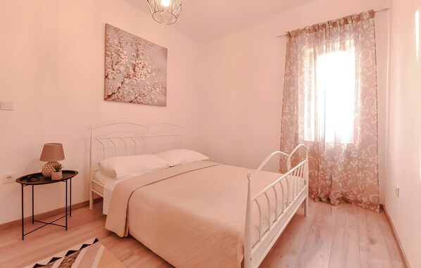 A bedroom with a bed, a bedside table with a lamp, a painting on the wall, and a window with curtains.