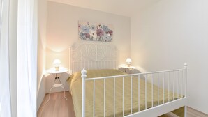 Een slaapkamer met een bed met een wit metalen frame, een groene spreidek, twee bedlampen en een bloemrijk kunstwerk boven het bed.