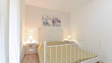 A bedroom with a white metal bed frame, a green bedspread, two bedside lamps, and a floral wall art piece above the bed.