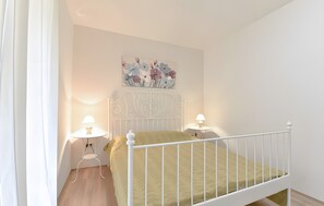 A bedroom with a white metal bed frame, a green bedspread, two bedside lamps, and a floral wall art piece above the bed. - Apartment '2' with Sea View, Shared Terrace and Wi-Fi (Sveti Petar na Moru)