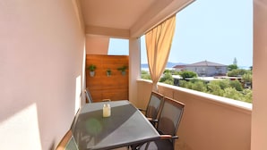 Een balkon met een tafel en stoelen, een houten muur met planten en uitzicht op huizen en bomen.
