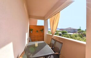 A balcony with a table and chairs, a wooden wall with plants, and a view of houses and trees. - Apartment '2' with Sea View, Shared Terrace and Wi-Fi (Sveti Petar na Moru)
